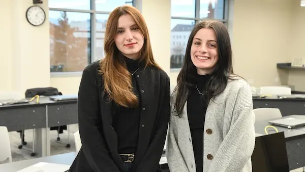 Two female college students standing in a classroom.